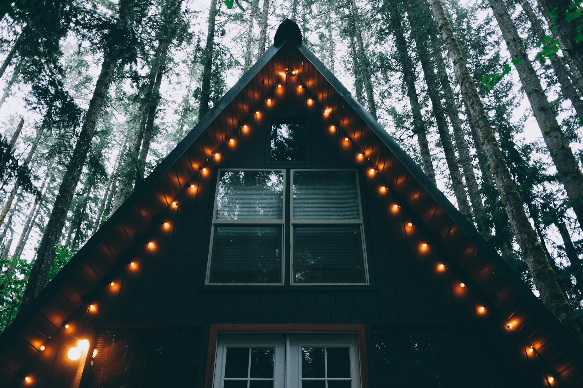 A-frame домик с тёплой гирляндой огней в вечернем сосновом лесу